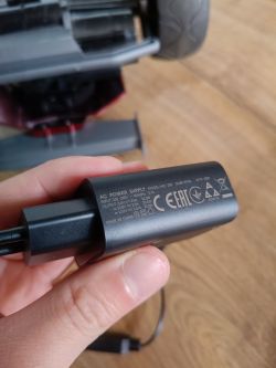 Zasilacz AC Power Supply Model LMC-26L trzymany w ręce, widoczna specyfikacja techniczna.