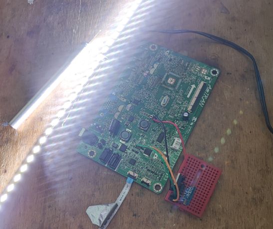 Circuit Board and LED Strip on Wooden Surface A circuit board with a WiFi module and a glowing LED strip on a wooden surface.