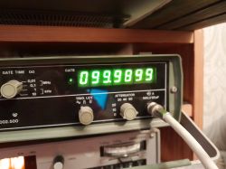 Częstotliwościomierz pokazujący 99,9899 MHz z podłączonym przewodem koncentrycznym