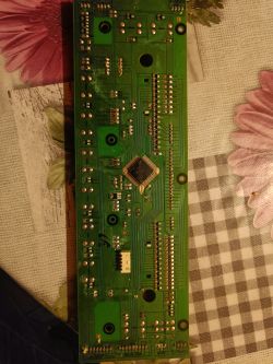 Zielona płytka drukowana z różnymi komponentami elektronicznymi, umieszczona na stole z kwiatowym obrusem.
