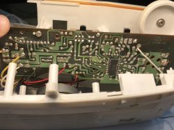 Bottom side of a PCB inside a white radio casing, showing traces, solder joints, an IC, and wires