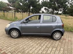 A blue car parked on a paved surface with trees in the background.