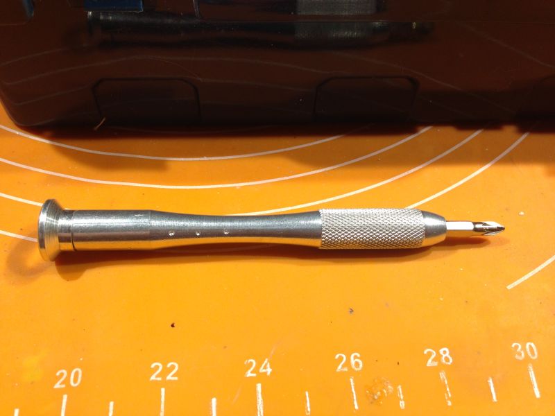 Metalowy wkrętak ręczny na pomarańczowej macie.