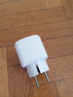 A white smart plug lying on a wooden floor.