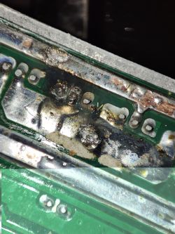 Zbliżenie na uszkodzony obwód elektroniczny z widocznymi śladami przypaleń i zwarć w okolicy tranzystorów.