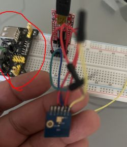 A hand holding a sensor module connected with wires to a breadboard with a power supply.