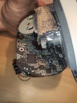 Rozebrane urządzenie elektroniczne z widoczną płytką drukowaną i torebką z granulatem.