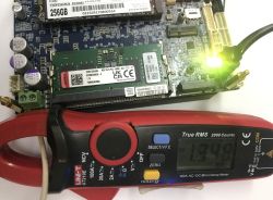 Płyta główna z modułem RAM i świecącą diodą, na dole multimetr cęgowy UNI-T