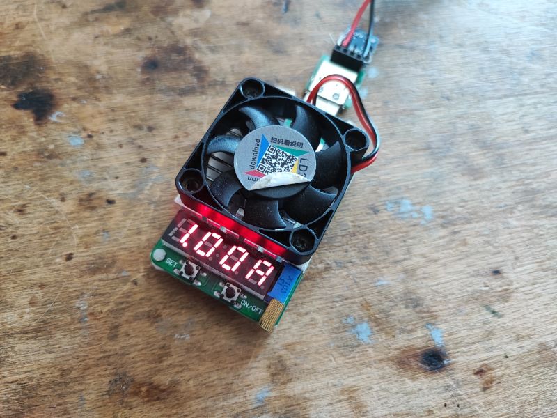 Sztuczne obciążenie elektroniczne z wyświetlaczem LED na drewnianym blacie.