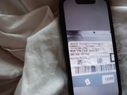 Ekran telefonu z fotografią etykiety radia Kia z kodem kreskowym na tle jasnej tkaniny.