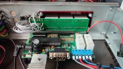 Widok wnętrza obudowy urządzenia elektronicznego z widoczną płytką PCB, kablami i podzespołami, takimi jak kondensatory, przekaźniki i radiator.