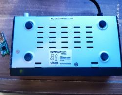 Tył tunera WIWA H.265 MAXX z widocznymi otworami wentylacyjnymi, informacjami o modelu i numerze seryjnym. Obok leży mały komponent elektroniczny.
