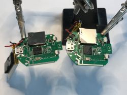 Two printed circuit boards with mounted electronic components held by metal laboratory clamps.