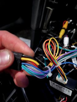 Osoba trzymająca wiązkę kolorowych przewodów w samochodzie obok kostki elektrycznej.