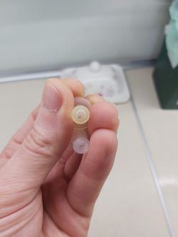 Osoba trzymająca w ręku dwa małe, plastikowe elementy rurki.