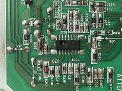 Zbliżenie na zieloną płytkę drukowaną z różnymi elementami elektronicznymi, w tym uszkodzonym scalakiem.