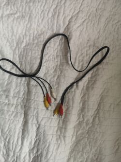 Kabel RCA z trzema końcówkami w kolorach: czerwonym, żółtym i białym, leży na białym kocu.