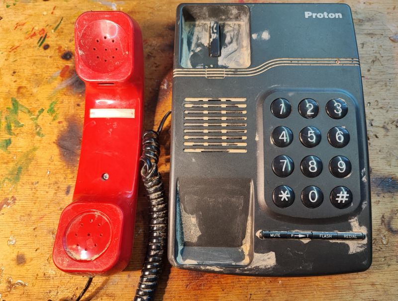 Telefon stacjonarny Proton T1332 z lat 90. z czerwoną słuchawką i czarną obudową.