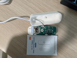 Disassembled water leak sensor with exposed PCB and cable on a wooden tabletop