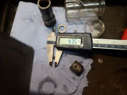 Suwmiarka mierzy kulkę o średnicy 4,75 mm, leżącą na niebieskim ręczniku papierowym wśród elementów metalowych.