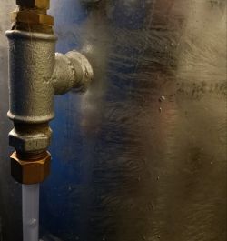 Zbliżenie na metalową rurkę z czarnym tłem, ukazującą element instalacji hydraulicznej.