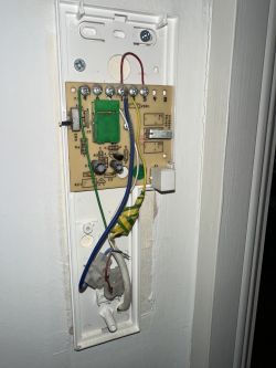 Exposed circuit board with wires in an open wall-mounted enclosure.