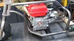 Motor mit rotem Kraftstofftank in Metallrahmen eines kleinen Dreirads montiert.
