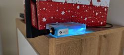 Zigbee Gateway with blue lighting on a wooden shelf next to a festive box.