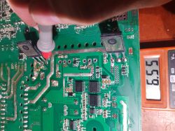 Voltage measurement on a green circuit board using a probe and a meter displaying 6.55 V.