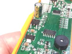 Zbliżenie na płytkę drukowaną stacji lutowniczej z widocznymi elementami elektronicznymi: stabilizatory AMS1117 i 78M09, kondensator elektrolityczny, układ scalony 74HC164D oraz buzzer.