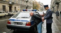 Police officer handcuffing a man leaning on a FSO Polonez patrol car with plate WAG 1234