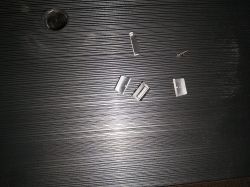 Połamane plastikowe zatrzaski leżące na czarnej, prążkowanej powierzchni.