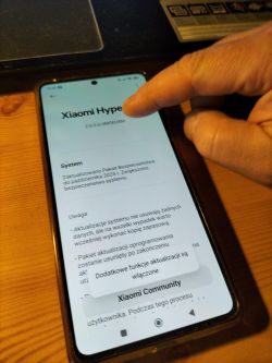 Palec wskazuje ekran telefonu Xiaomi na stronie informacji o systemie HyperOS