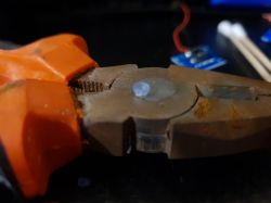 Szczypce trzymające małą, przezroczystą gumkę z przycisku gimbalu.