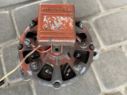 Widok alternatora Motorola z widoczną zdejmowaną pokrywą i przewodami, umieszczony na kostce brukowej.