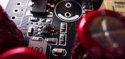 Zbliżenie na płytkę drukowaną z czerwonymi kondensatorami i elementem elektronicznym.