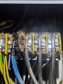 Spalona instalacja elektryczna z widocznymi kablami i zaciskami.