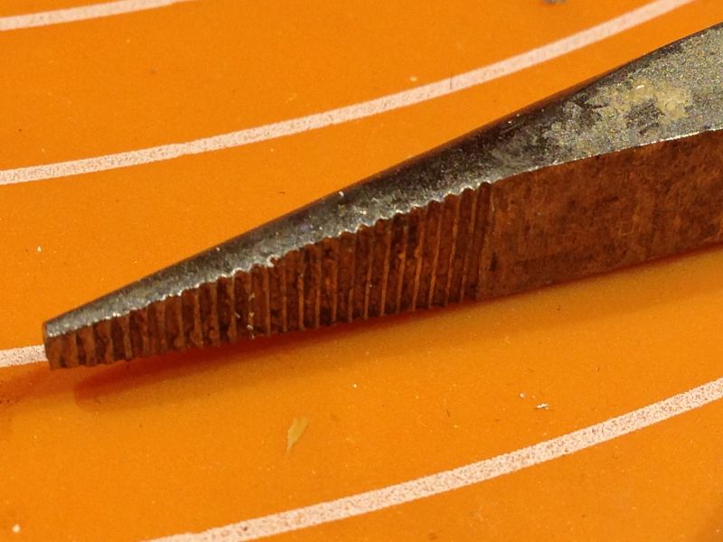 Zbliżenie na zużytą końcówkę szczypiec z wyraźnym ząbkowaniem.