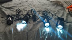 Four LED spotlights with cables on a bed, three of which emit blue light.