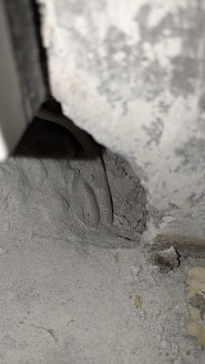 Przewody elektryczne wystające spod tynku w betonowej posadzce.
