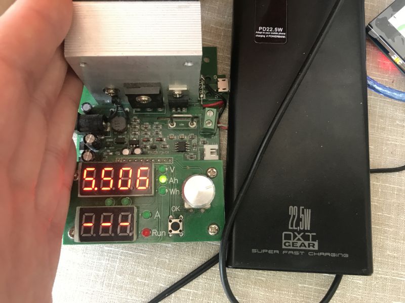 Electronic tester showing 5.506 V and NXT Gear 22.5 W power bank during charging test