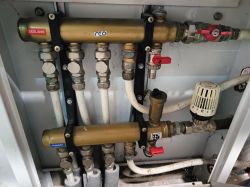 Mosiężny rozdzielacz ogrzewania z czterema wyjściami, zaworami i głowicą termostatyczną w szafce