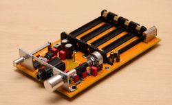 Headphone amplifier on a yellow circuit board with slots for four cells.