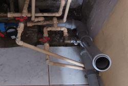 Rury instalacyjne w łazience z szarą rurą odpływową i zaworami.