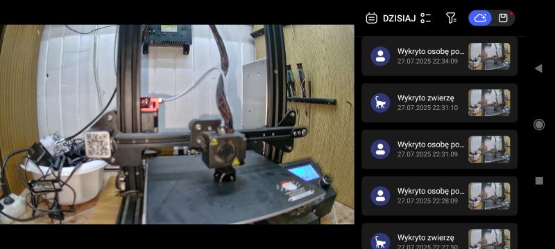 Drukarka 3D w pomieszczeniu z ekranem interfejsu na urządzeniu mobilnym.
