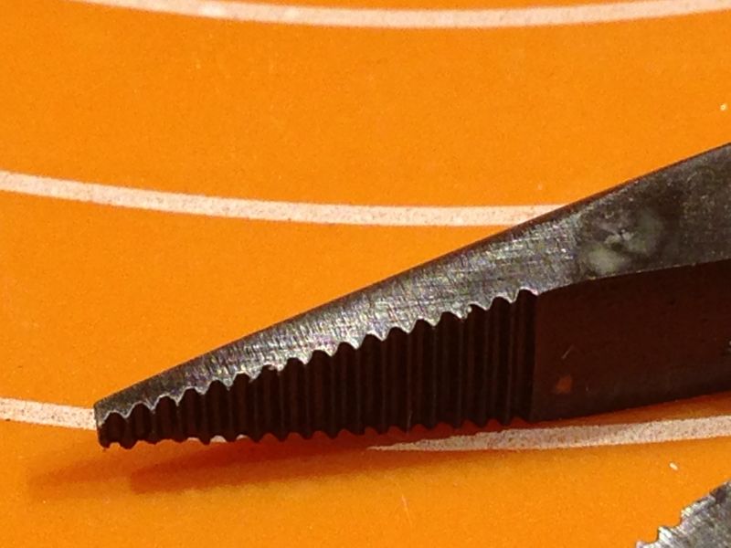 Makro zbliżenie na ząbkowaną szczękę kombinerek na pomarańczowym tle.