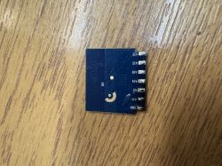 Blue PCB module with labeled signal pins resting on a wooden surface
