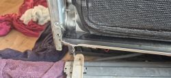 Woda kapie z dolnej krawędzi drzwi zmywarki z odkrytą izolacją i metalową ramą