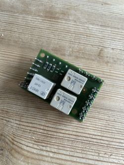 A circuit board with mounted relays lying on a wooden surface.