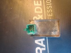 Zielony wtyk elektryczny podłączony do prostokątnego, metalowego urządzenia na ciemnym tle.